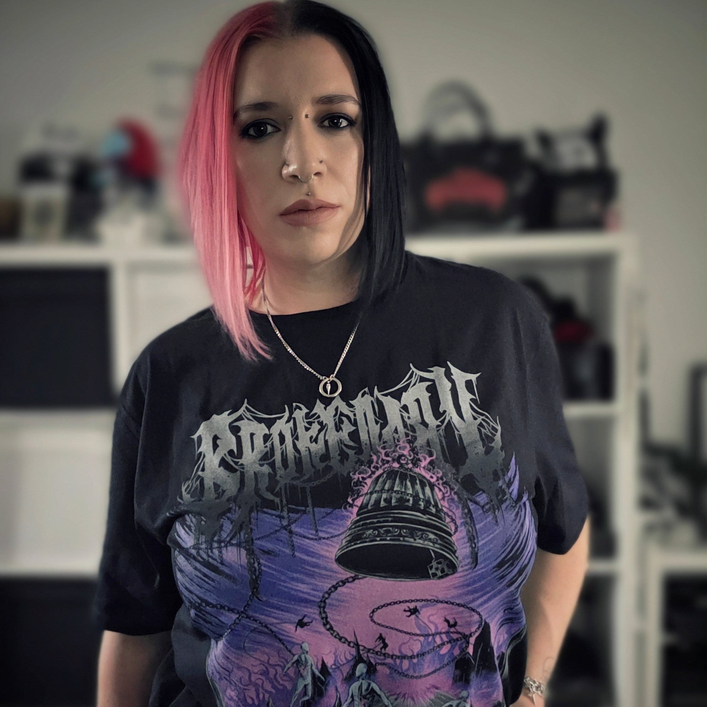 Person wearing a black t-shirt with graphic design and text, standing indoors.