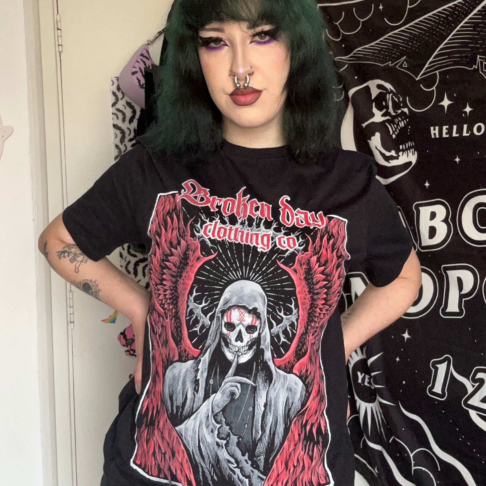 A person wearing a black t-shirt with a graphic design of a character in red and white, standing in front of a mirror.