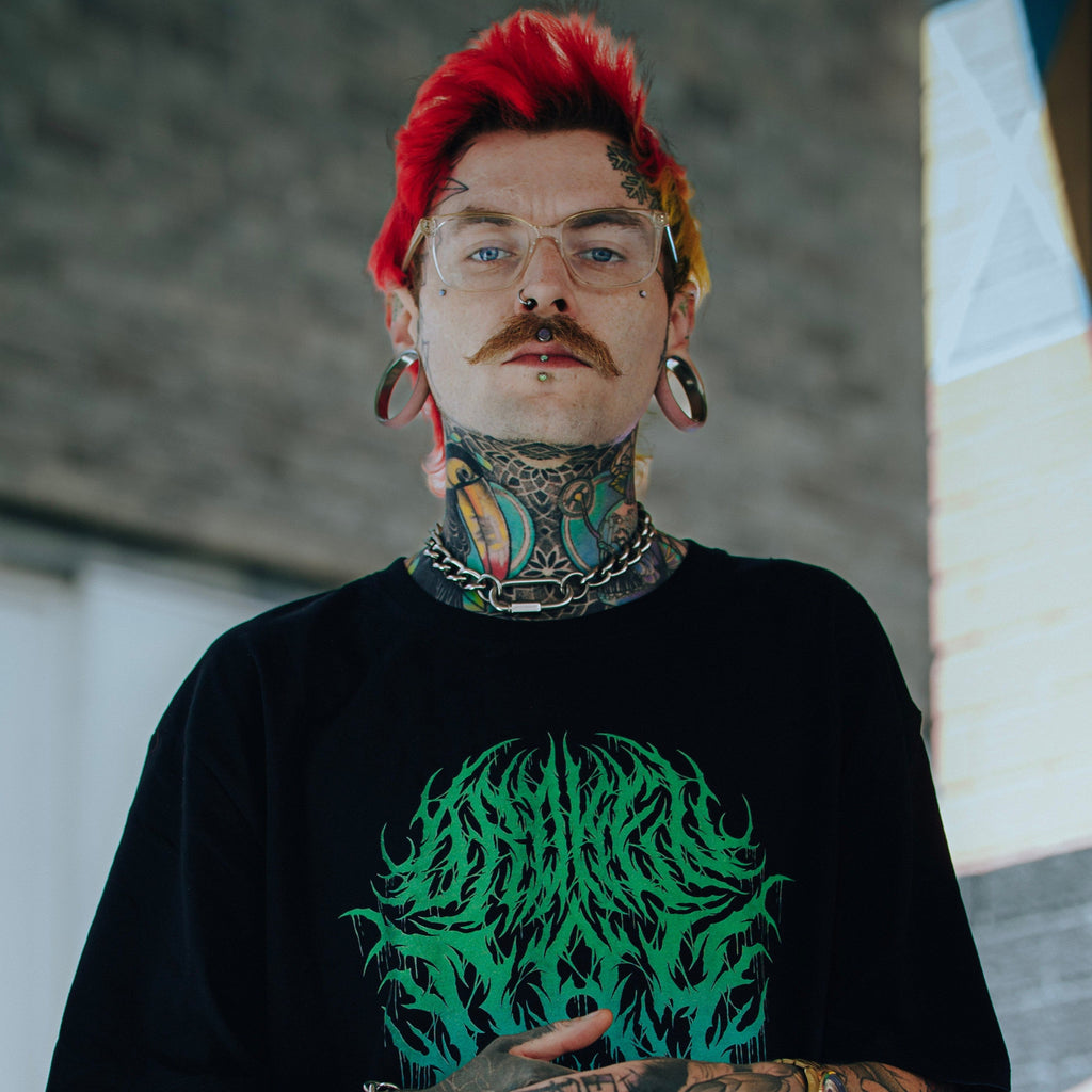 Man with tattoos wearing a black t-shirt with a green graphic design.