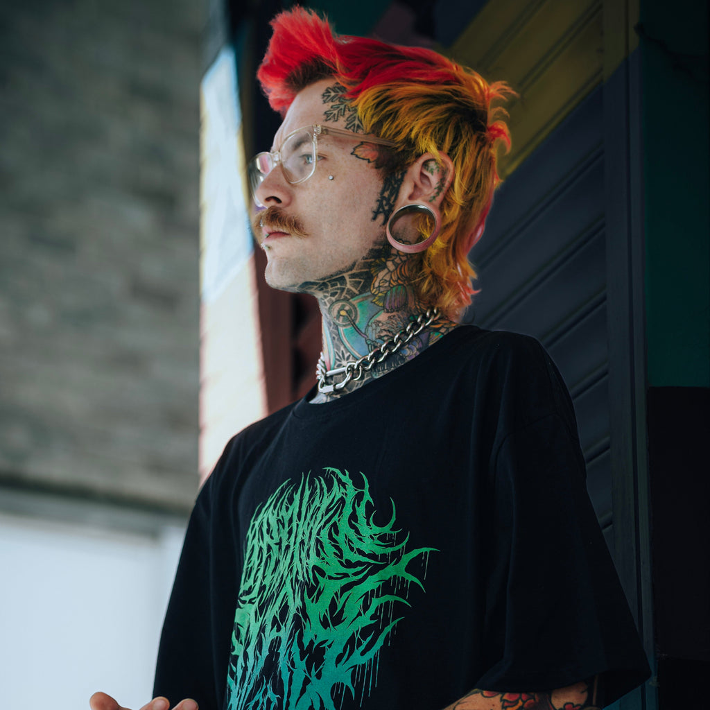 Person with tattoos wearing a black t-shirt with a green graphic design.