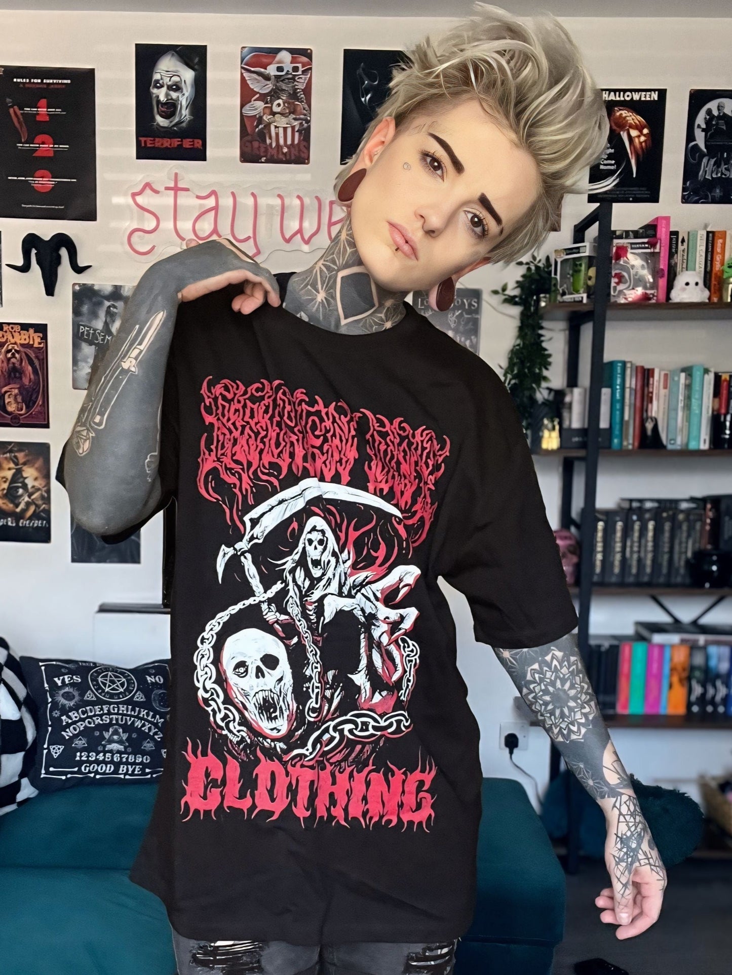 Person wearing a black graphic t-shirt in a room with posters and books on the wall.